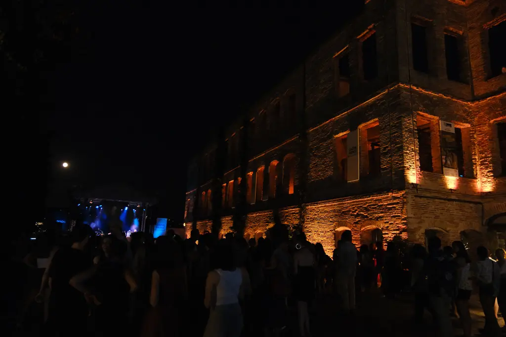 Gece Esma Sultan Yalısı'nın önünde kalabalık; aydınlatılmış duvarlar, solda mavi sahne ışıkları ve ay.