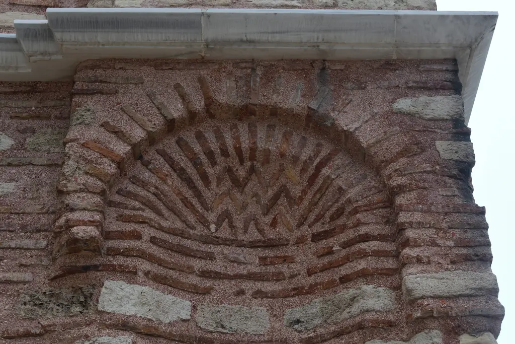 Fenari İsa Camii'nin batı cephesinde tek bir kör kemer nişi; kemerin içi yelpaze biçiminde ışınsal tuğlayla doldurulmuş, üstte beyaz mermer korniş uzanıyor.
