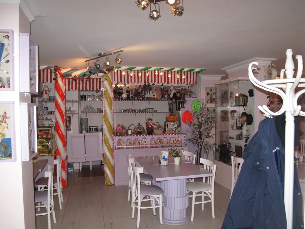 İstanbul Oyuncak Müzesi'nde Müze Cafe; beyaz masalar ve sandalyeler, kırmızı beyaz çizgili sütunlar ve oyuncaklarla dolu raflar.