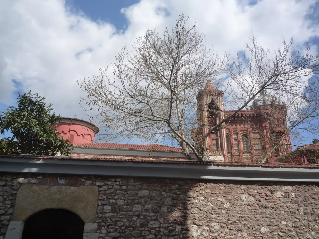 Kanlı Kilise'nin çevre duvarı; kemerli kapı, yapraksız büyük bir ağaç, solda kırmızı kubbe ve arkada Fener Rum Erkek Lisesi'nin kulesi.