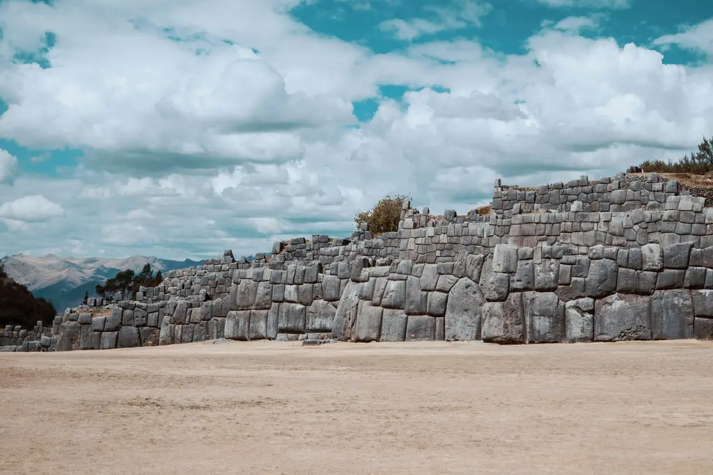 Cusco üzerinde Sacsayhuamán; zikzak biçiminde dizilmiş dev taş bloklardan oluşan İnka duvarları ve çim alan.