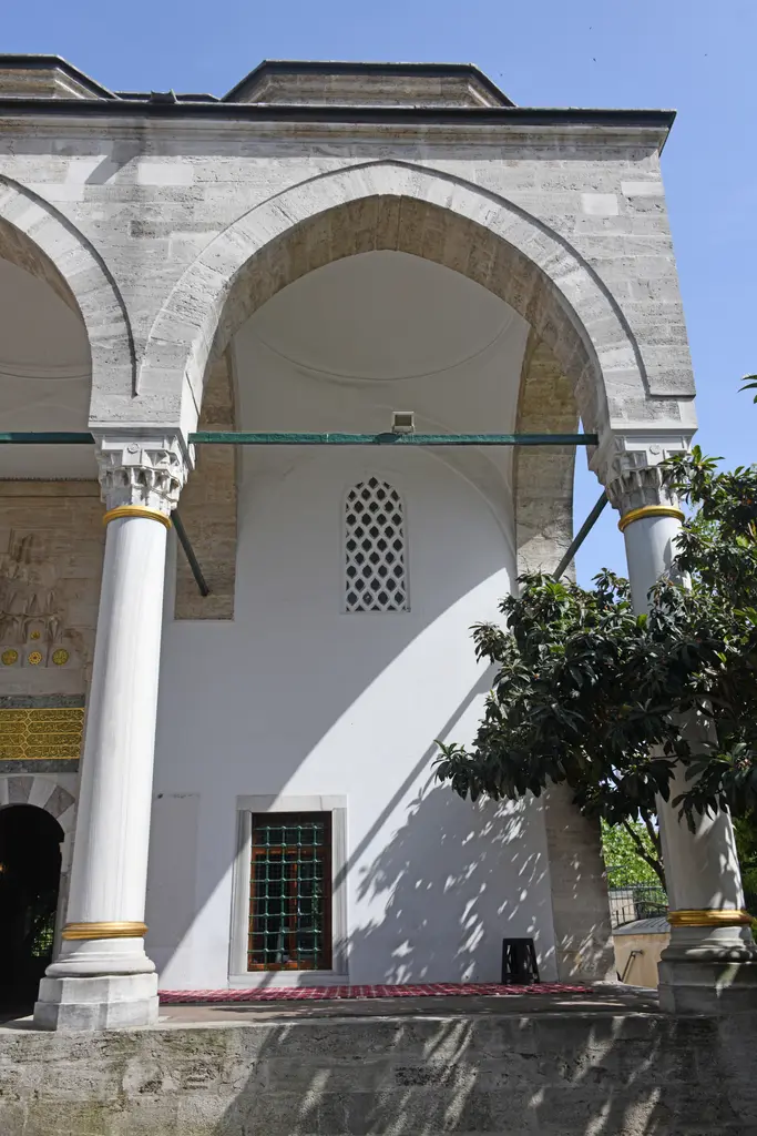 Firuz Ağa Camii'nin revakı yandan; sivri kemerler, mermer sütun başlıkları, beyaz badanalı duvar ve alt pencereler.