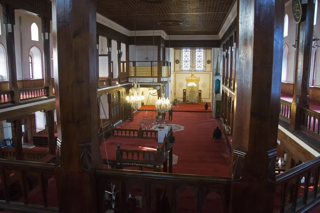 Arap Camii'nin içi; ahşap direkler ve korkuluklarla çevrili iki katlı mahfiller, kırmızı halı ve uzakta aydınlık mihrap.