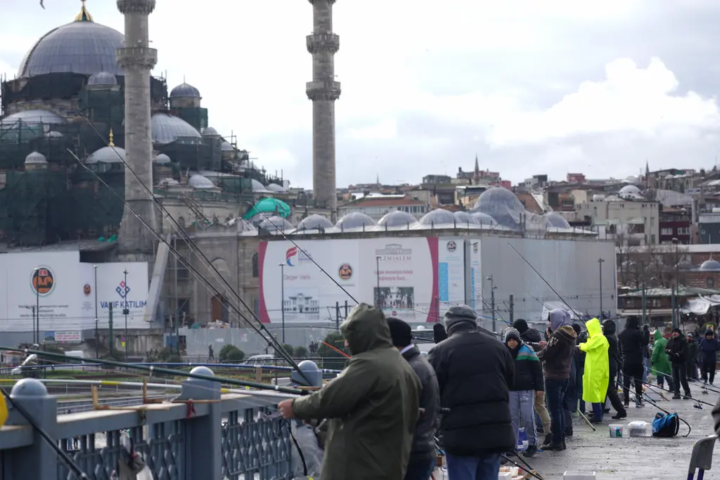 Kışın köprüde kalabalık balıkçılar; montlu insanlar, oltalar, solda cami kubbeleri ve arkada binalar.