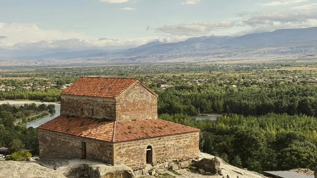 Uplistsikhe'de kayaya oyulmuş antik kent; taş odalar, geçitler ve tepede kırmızı çatılı küçük bir kilise.