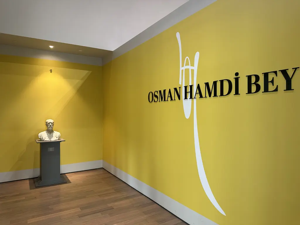 İstanbul Resim ve Heykel Müzesi'nde sarı duvarlı bir sergi girişi; büyük siyah harflerle Osman Hamdi Bey yazısı ve kaide üstünde büst.