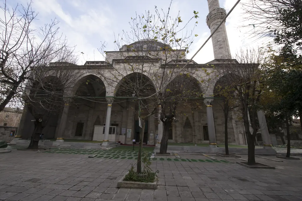Gazi Atik Ali Paşa Camii'nin son cemaat yeri; beş sivri kemer, sütunlar, arkada kubbe ve minare, önde ağaçlar ve taş avlu.