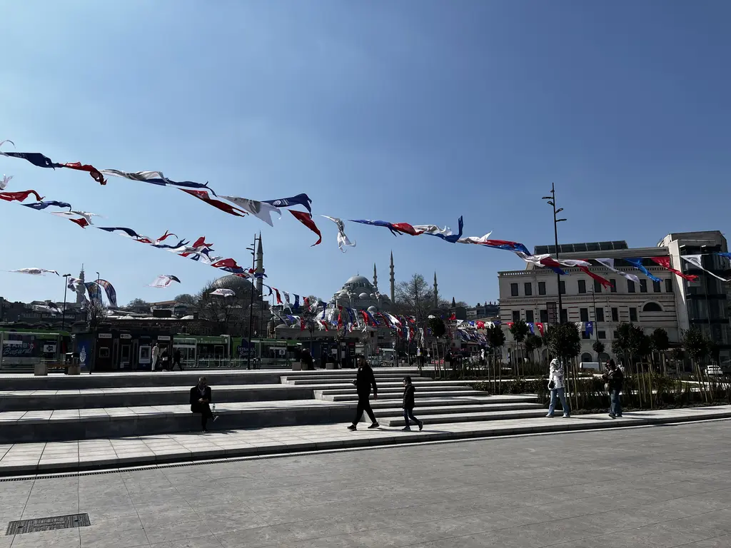 Eminönü meydanı; geniş taş basamaklar, gergin ipler üzerinde flamalar, solda Yeni Cami'nin kubbeleri ve sağda tarihî bina.