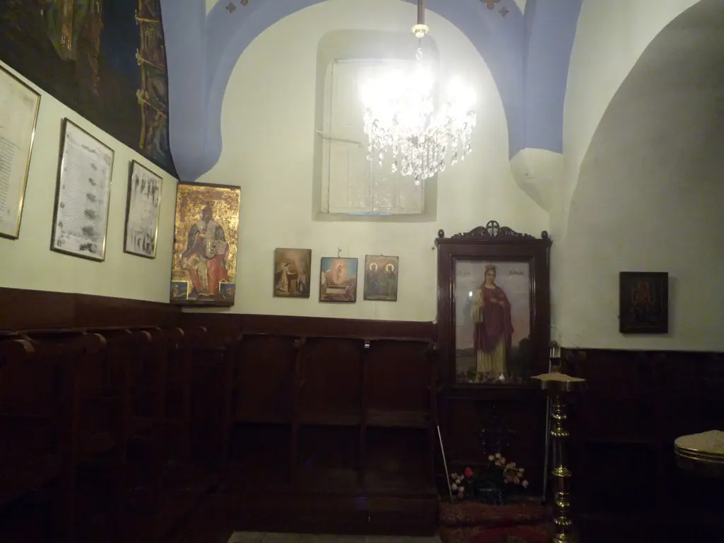 Kanlı Kilise'nin iç duvarı; çerçeveli belgeler, küçük ikonalar, ahşap koltuklar, ayaklı bir ikona dolabı ve tavandan sarkan avize.