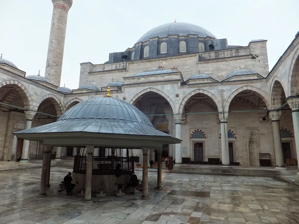 Yavuz Sultan Selim Camii'nin avlusu; mermer zemin, ortada kurşun çatılı şadırvan, çevresinde sütunlu revak kemerleri, arkada kubbe ile minare.