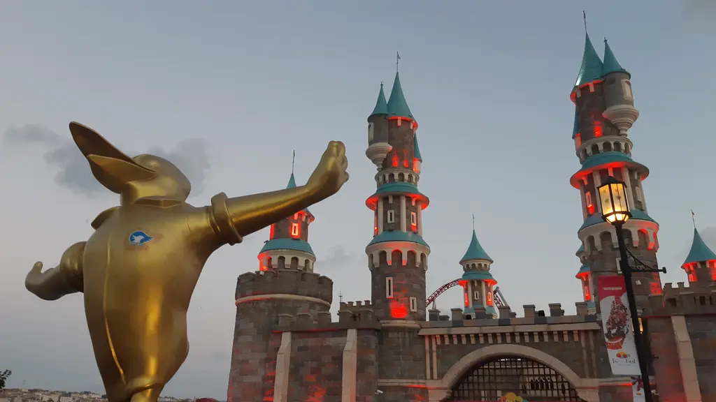 Vialand'de yakından altın renkli tavşan kulaklı maskot heykeli; arkada kırmızı ışıklı şato kuleleri ve akşamüstü gökyüzü.