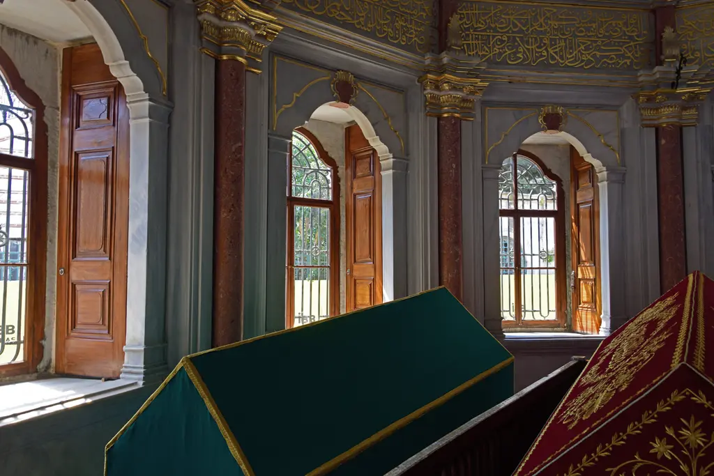 Mihrişah Valide Sultan Türbesi'nde sandukalar; yeşil ve kırmızı örtüler, ahşap kanatlı pencereler, pembe sütunlar ve yaldızlı kuşaklar.
