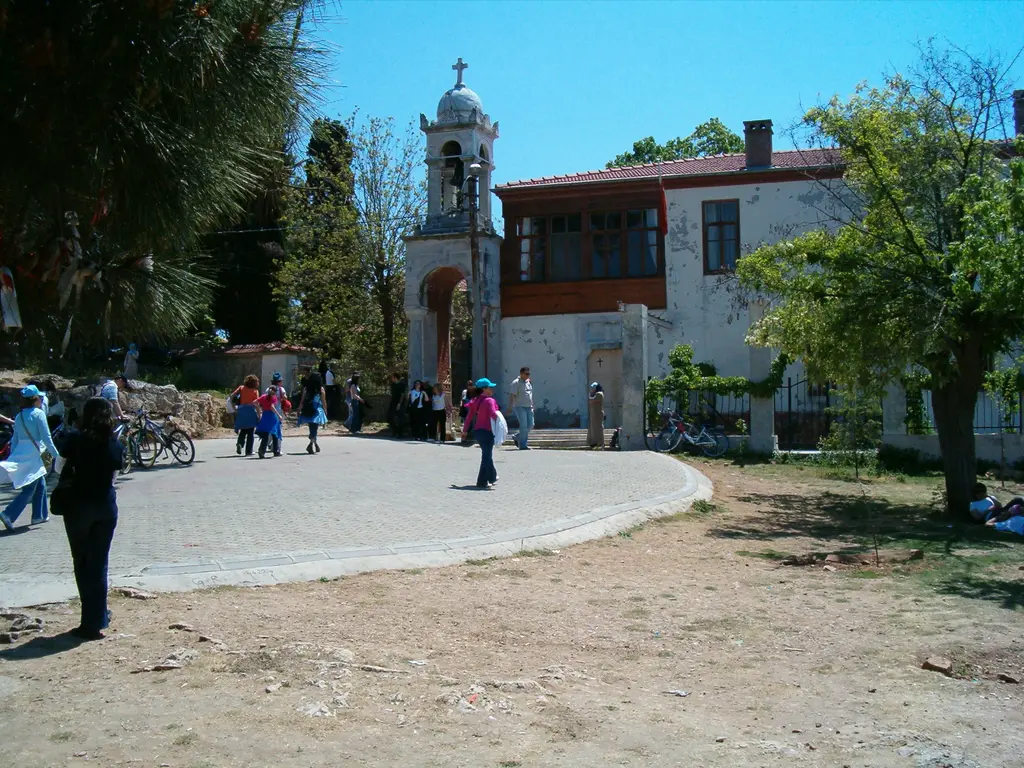 Büyükada'da Aya Yorgi Manastırı; tepedeki taş kilise ve ek binalar, çevresinde ağaçlar ve mavi gökyüzü.