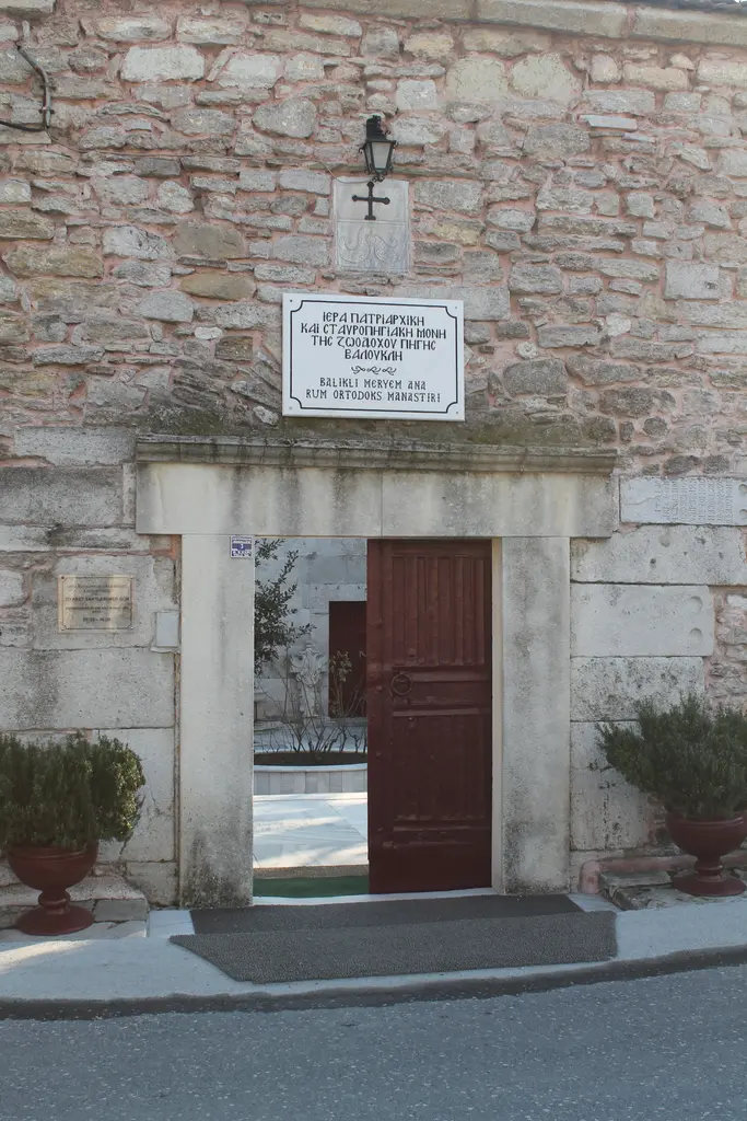 Manastırın sokak kapısı; moloz taş duvar, mermer söveli açıklık, bordo ahşap kanat ve üstünde iki dilde yazılmış mermer levha ile küçük haç.
