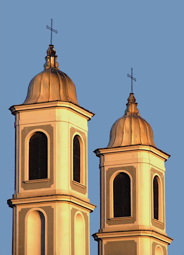 Notre Dame de l'Assomption Kilisesi'nin çan kuleleri; turuncu ışık alan iki kule, kubbe başlıkları, haçlar ve mavi gökyüzü.