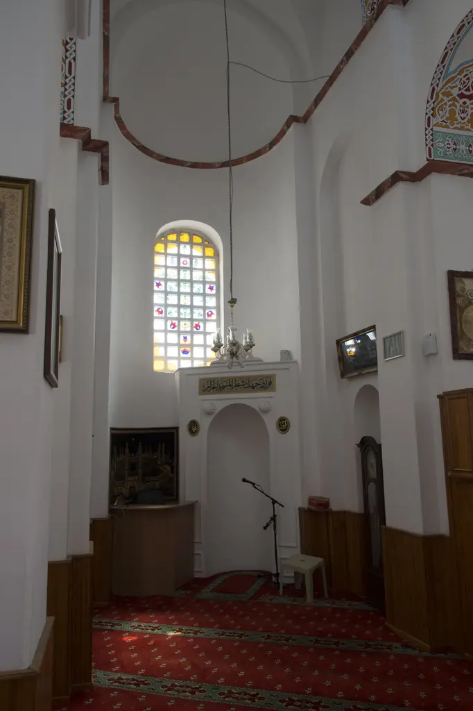 Bodrum Camii'nin mihrabı; sade beyaz niş, üstünde altın zeminli ayet kuşağı ve iki madalyon, yukarıda vitraylı kemerli pencere, solda Kâbe tablosu ve ahşap kürsü.