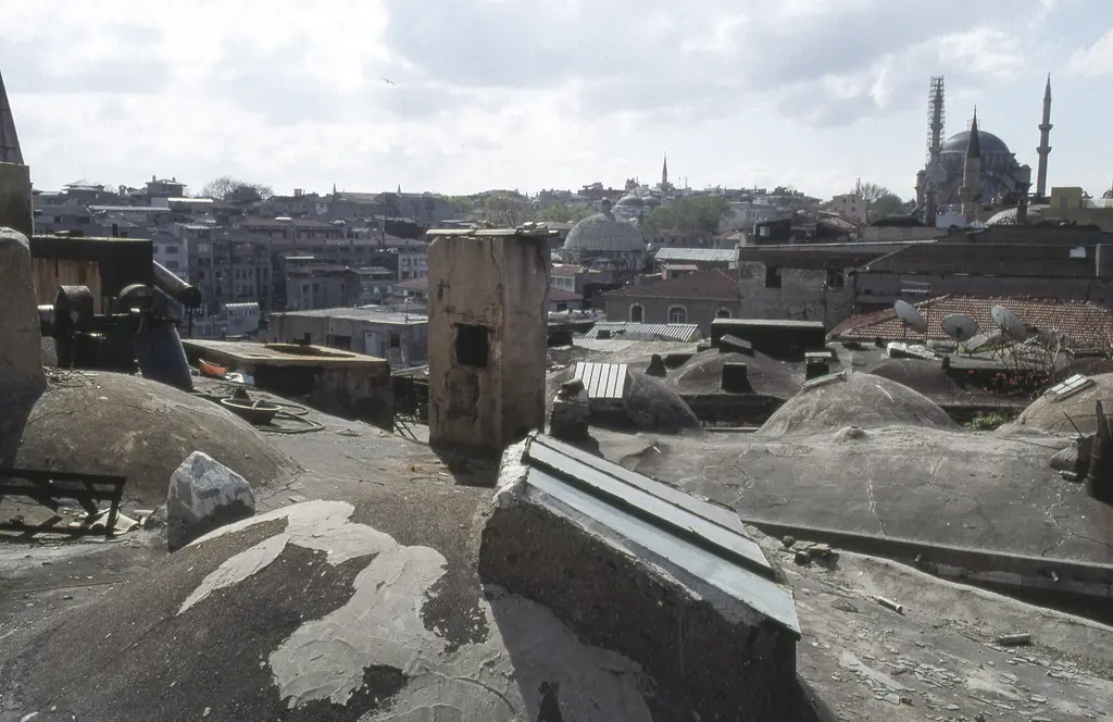 Büyük Valide Han'ın çatısı; önde harçla sıvanmış yayvan kubbe sırası, ortada kare taş baca, arkada kubbeleri ve minareleriyle tarihî yarımadanın silueti.