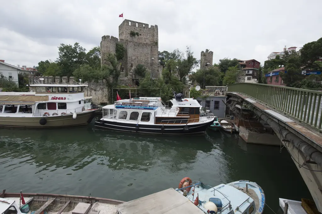 Göksu Deresi'nin ağzında tekneler; bağlı gezi tekneleri, köprü, arkada ağaçların arasından iç kale burcu.