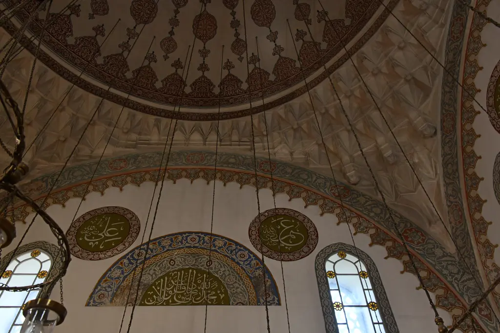 Firuz Ağa Camii'nin kubbesi içten; kırmızı ve kahverengi kalem işi desenler, yazı madalyonları, kemerler ve pencereler.