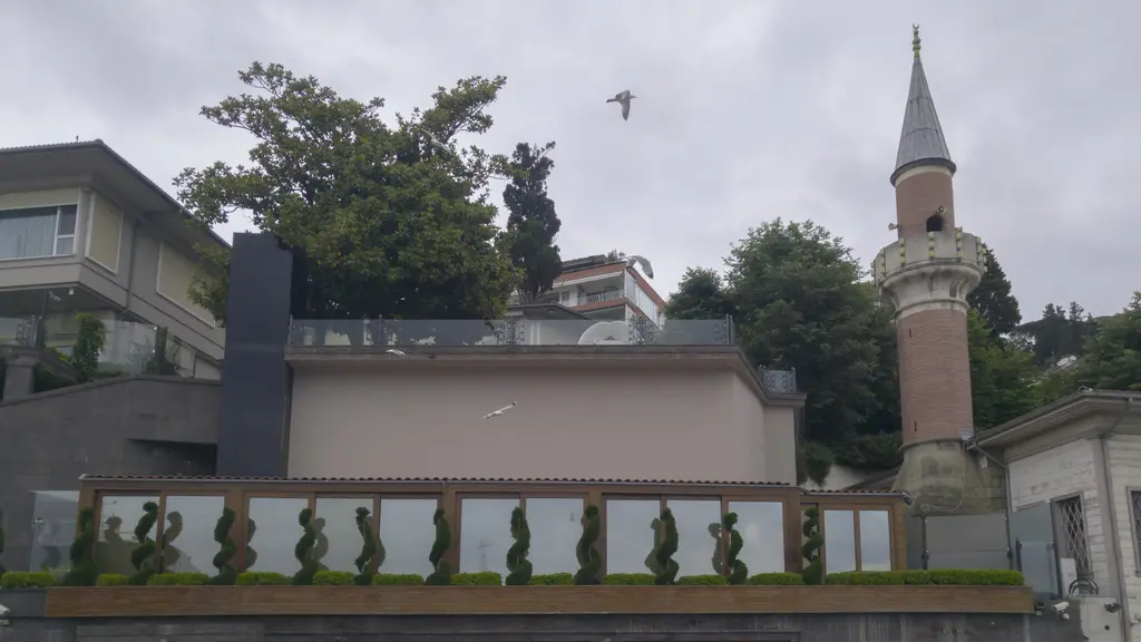 Kayalar Mescidi'nin minaresi; tuğla rengi gövde, sivri külah, yanında alçak duvar ve arkada ağaçlar.