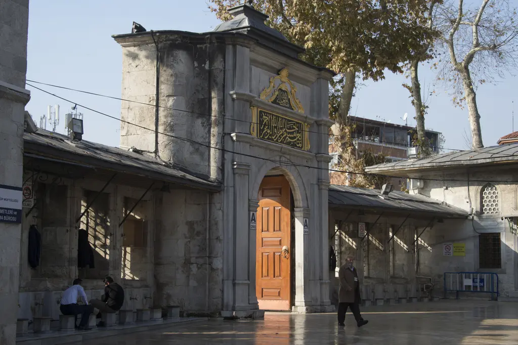 Eyüp Sultan Camii'nin dış avlu kapısı; kitabeli mermer taç kapı, ahşap kanatlar ve yanlarda kemerli pencereler.