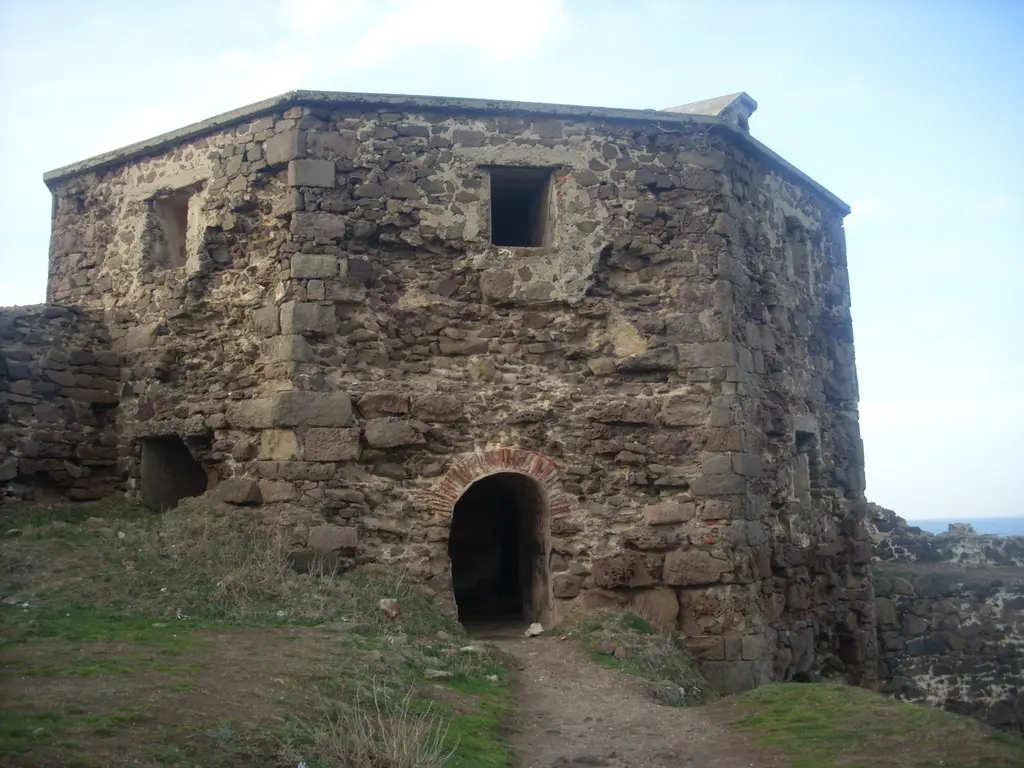 Rumeli Feneri Kalesi'nde taş yapı; kemerli kapılı kare bina, yıpranmış taş duvarlar ve çevresinde otlar.
