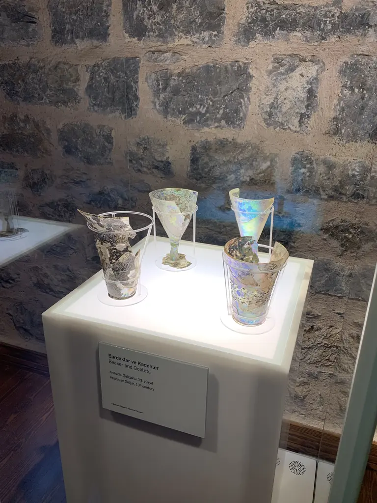 Beykoz Cam ve Billur Müzesi'nde aydınlatmalı bir kaide üzerinde kırık ve onarılmış, yanardöner yüzeyli cam bardak ve kadehler.