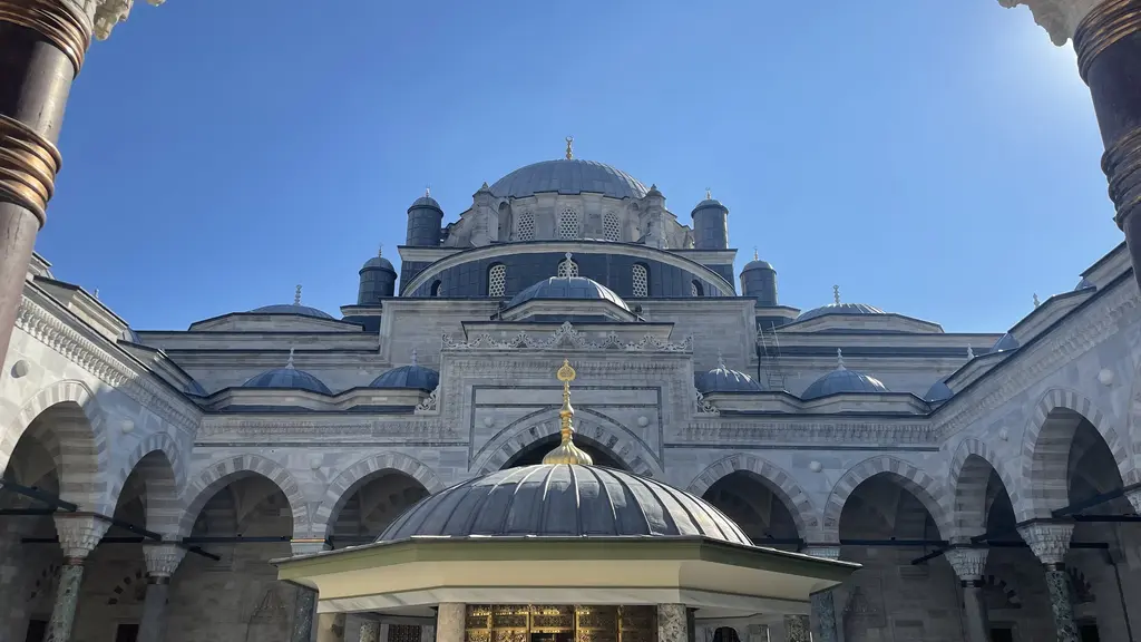 Avludan yukarı bakış; önde şadırvanın küçük kubbesi, arkada kademe kademe yükselen kubbeler ve mavi gökyüzü.