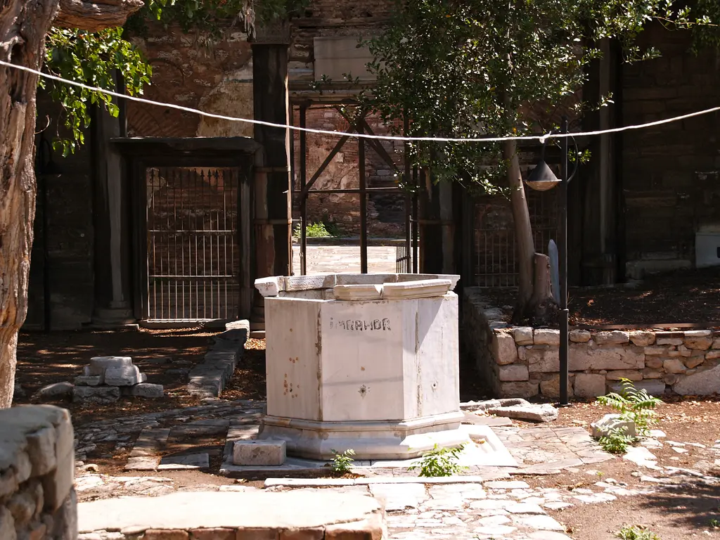 İmrahor İlyas Bey Camii'nin avlusunda sekizgen mermer şadırvan teknesi; gövdesinde İmrahor yazısı, arkada demir şebekeli kapılar, ahşap payandalar ve incir ağaçları.