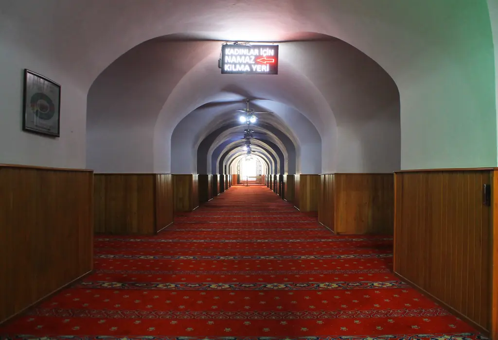 Yeraltı Camii'nde kırmızı halılı uzun bir sıra; beyaz badanalı tonozlar, sıralı kemerler ve uçta aydınlık giriş.