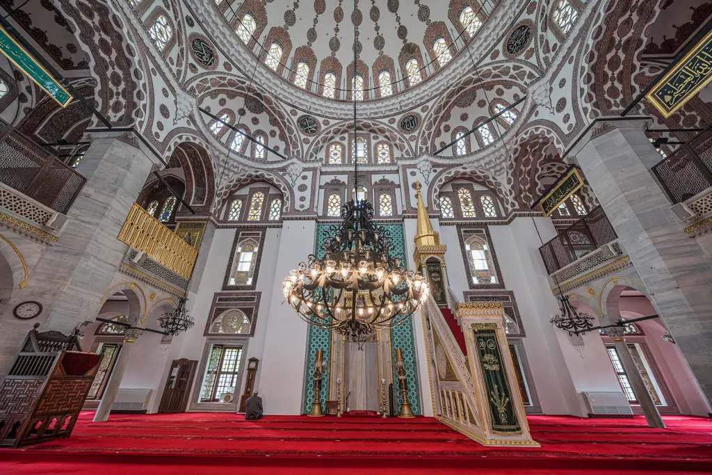 Yeni Valide Camii'nin içi; kırmızı halı, büyük avize, çinili mihrap, minber ve sütunlu mahfiller.