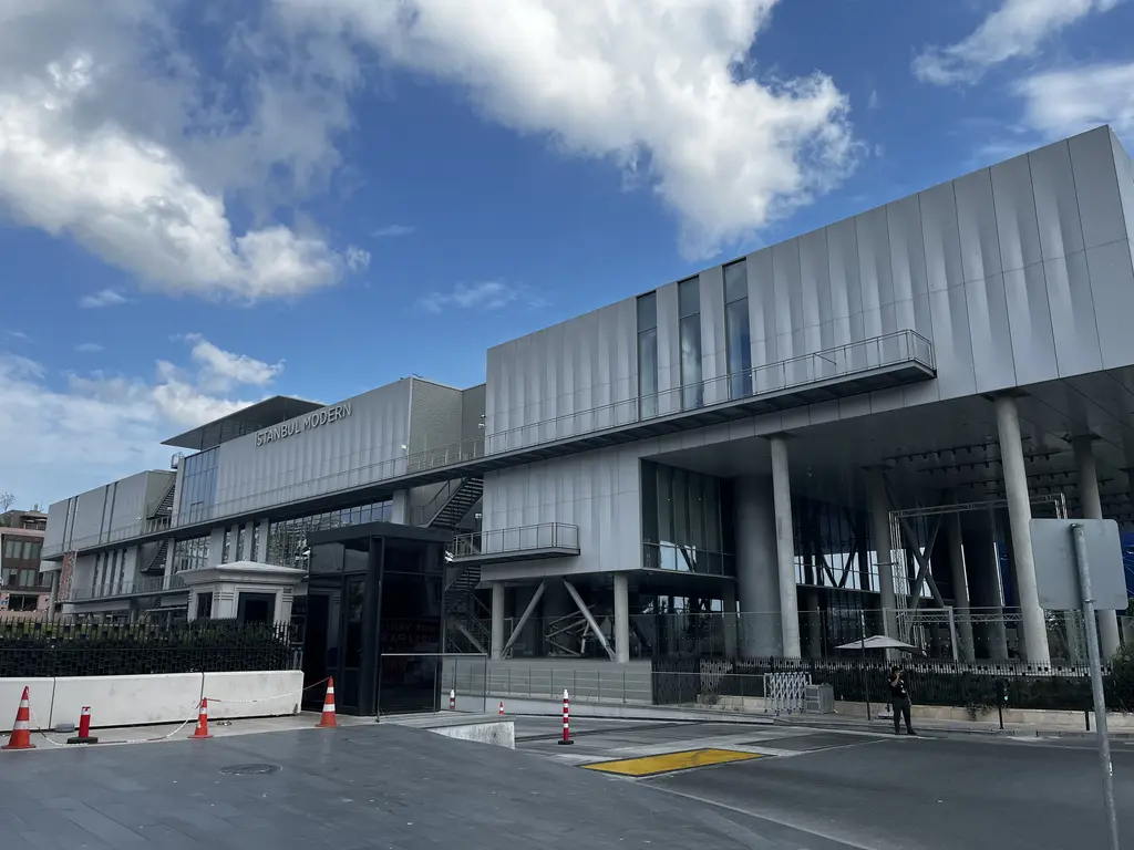 Kapalı bir günde İstanbul Modern; ince sütunlar üstünde yükselen kat, dış merdivenler ve önde beyaz bir heykel.