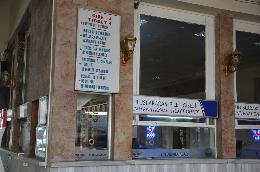Sirkeci Garı'nda kullanılmayan uluslararası bilet gişesi; mermer kaplı duvar, camlı beyaz çerçeveli gişe, mavi zeminli Türkçe İngilizce tabela ve üstte dört dilli kurallar panosu.