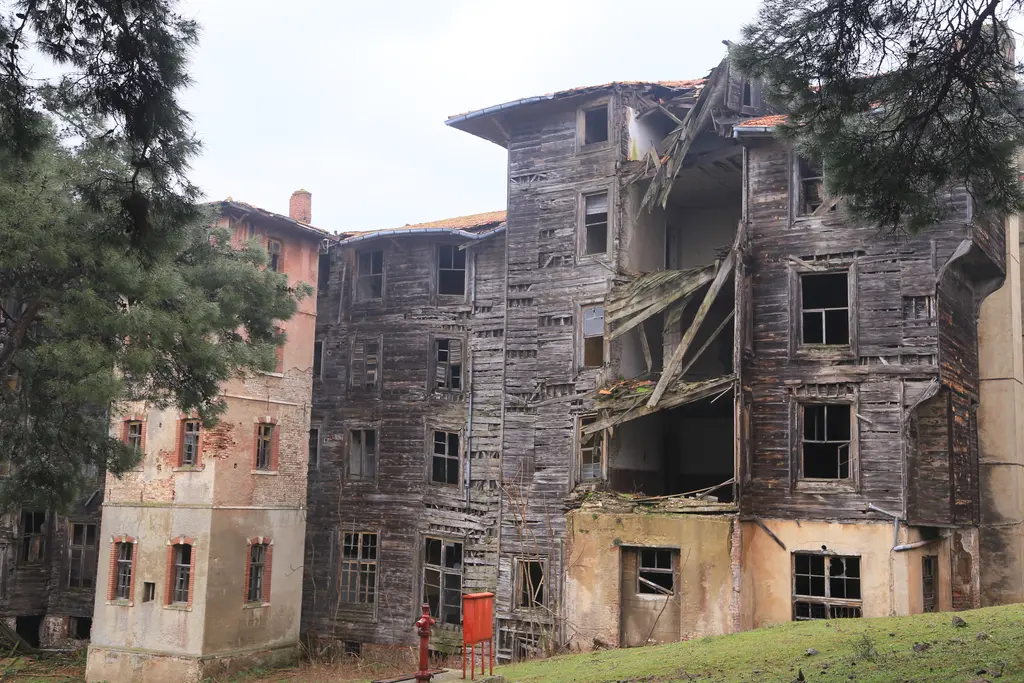 Büyükada Rum Yetimhanesi'nde yıkık katlar; sarkmış ahşap kaplama, boşalmış pencereler ve pembe sıvalı kanat.