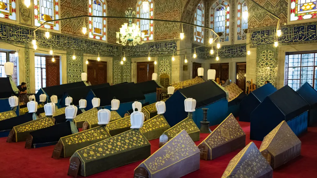 Sultan Ahmed Türbesi'nde renkli örtülü sandukalar; kırmızı halı üstünde yeşil, lacivert ve lila örtüler, beyaz sarıklar ve çini kaplı duvarlar.