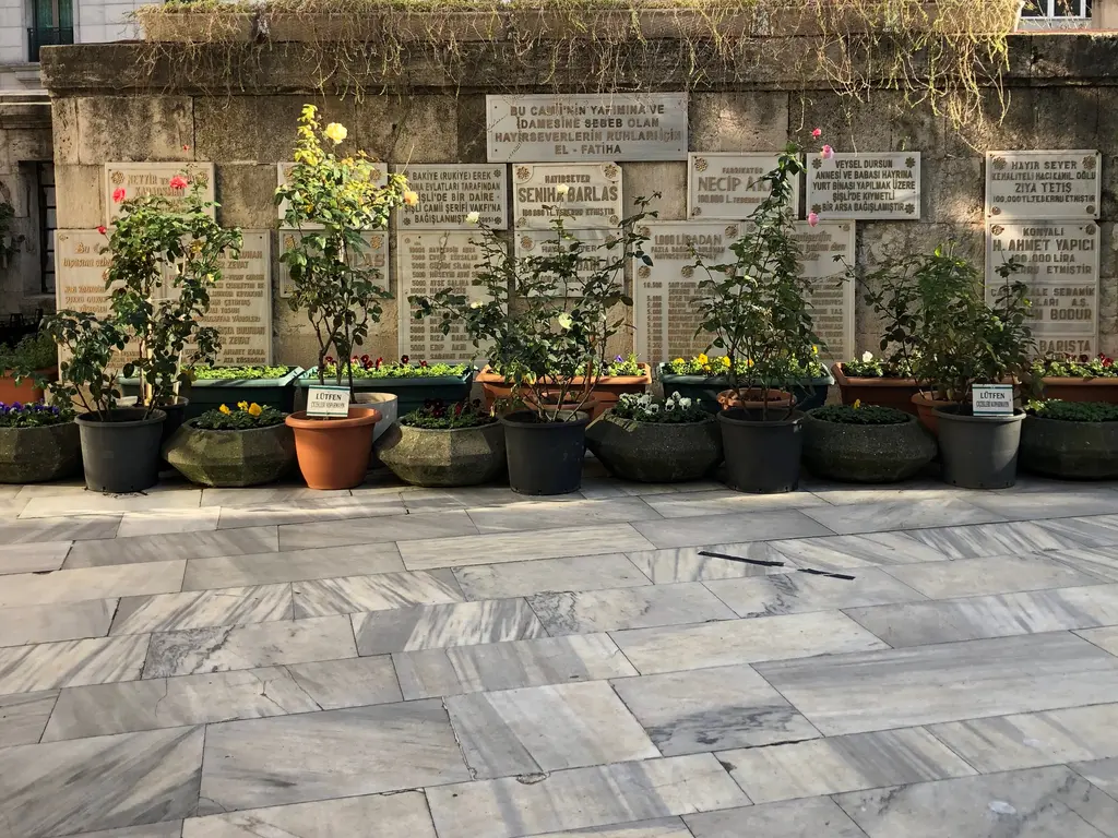 Şişli Camii'nin avlu duvarı; sıra sıra mermer levhalar, önünde saksılarda güller ve mermer döşeli avlu.