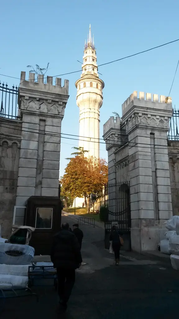 Beyazıt Kulesi bir kapı açıklığından; iki yanda dişli taş kuleler, demir parmaklık ve aradan görünen kulenin tam boyu.