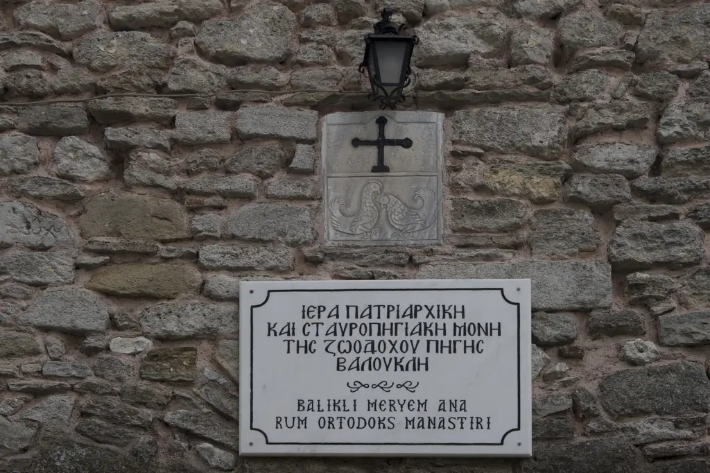 Manastırın taş duvarında mermer levha; üzerinde haç kabartması ile Rumca ve Türkçe yazı, yanında demir fener.