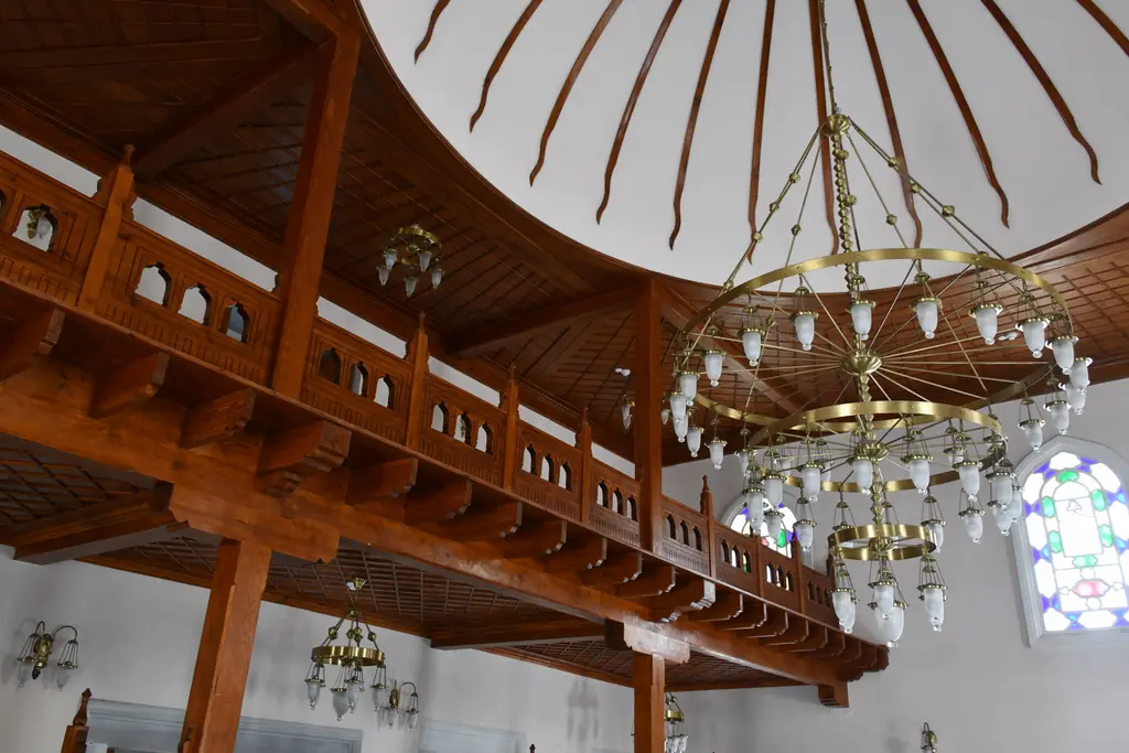 Şah Sultan Camii'nde mahfil; ahşap korkuluklu üst kat, dilimli kubbe, kristal avize ve renkli camlı pencere.
