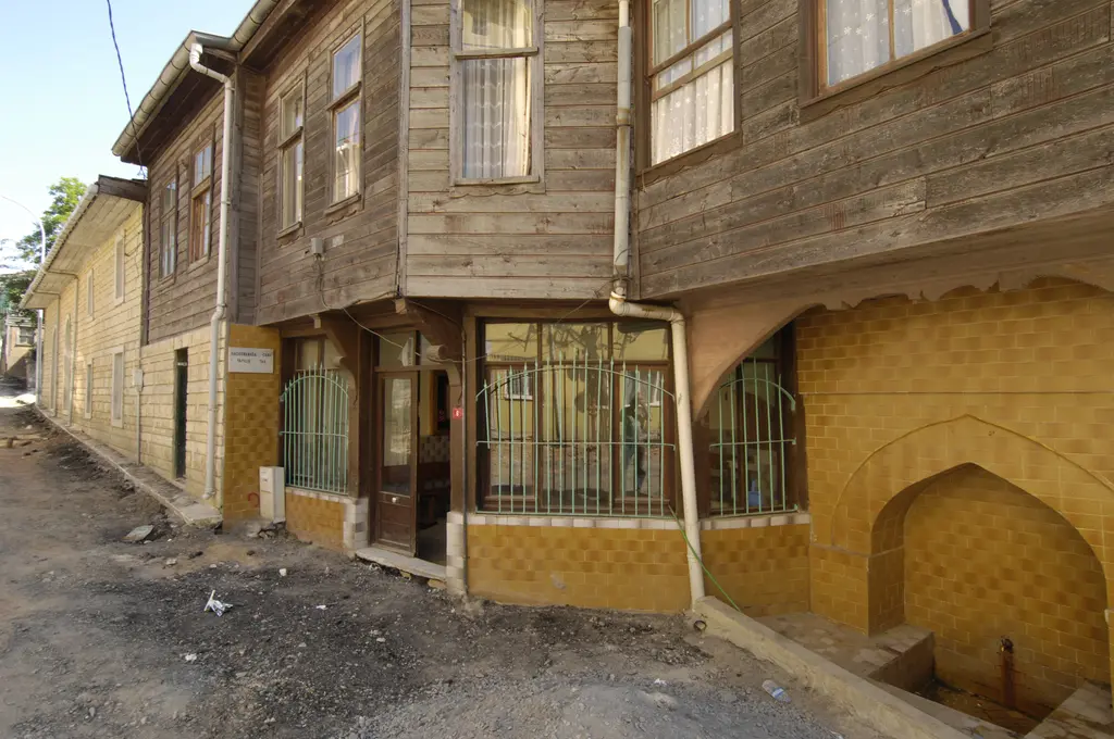 Şile'de bir sokak; ahşap çıkmalı ev, alt katta demir parmaklıklı pencereler ve sarı boyalı köşe duvarı.