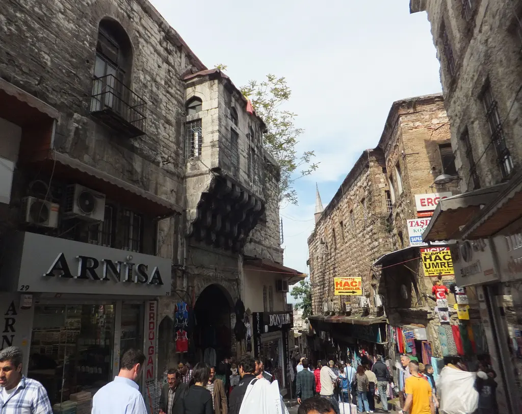 Mercan'da Çakmakçılar Yokuşu; iki yanda dükkânlar, sağda hanın taş cephesi ve ahşap çıkmaları, yokuş boyunca akan kalabalık.