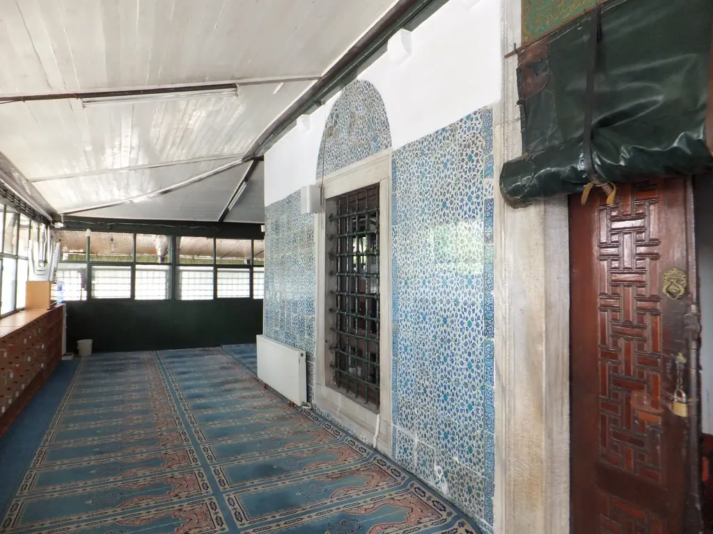 Çinili Camii'nin son cemaat yeri içi; halı serili zemin, çinili kuzey duvarı, pencere ve ahşap kapı kanadı.