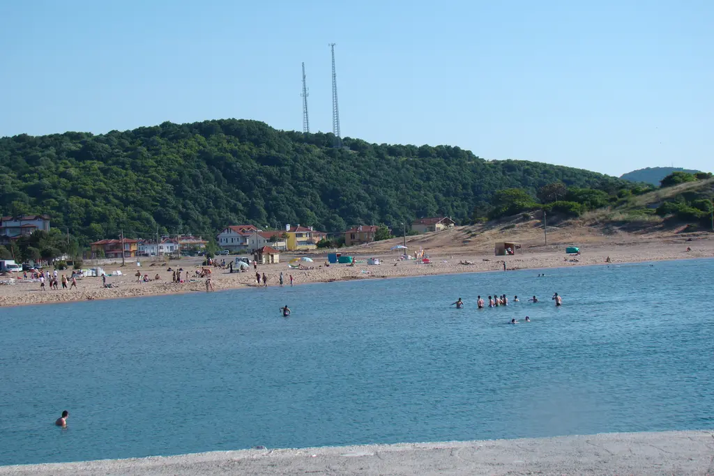 Ağva'da kumsal; yeşil tepelerin önünde kum şeridi, denizde yüzen insanlar ve tepede iki anten direği.