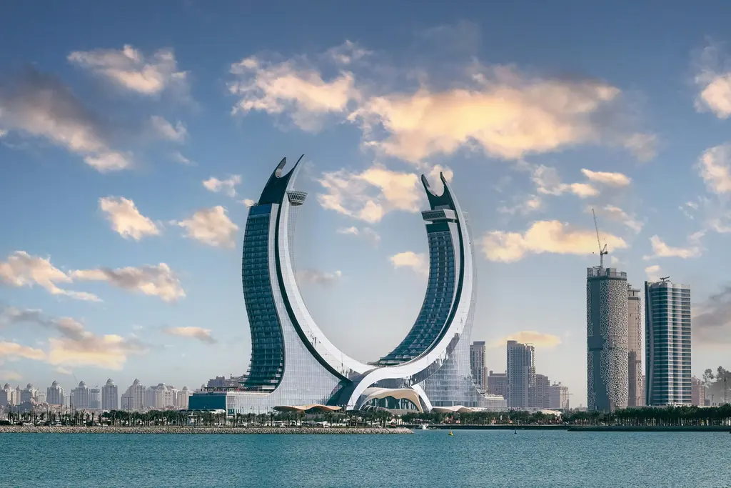 Lusail'de hilal biçiminde birbirine kenetlenen iki kule; kavisli beyaz gövdeleri, cam yüzeyleri ve çevresindeki alçak yapılar.
