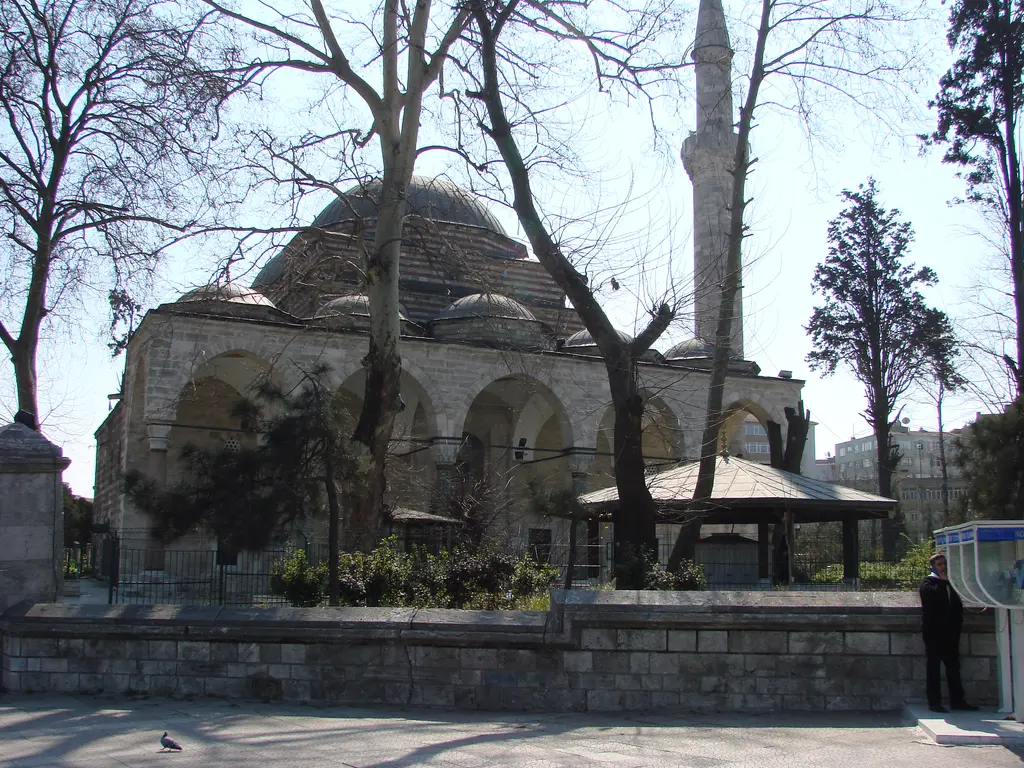 Murat Paşa Camii avlusu; kubbeli cami, kemerli son cemaat yeri, önde kubbeli şadırvan, yapraksız çınarlar ve alçak taş avlu duvarı.
