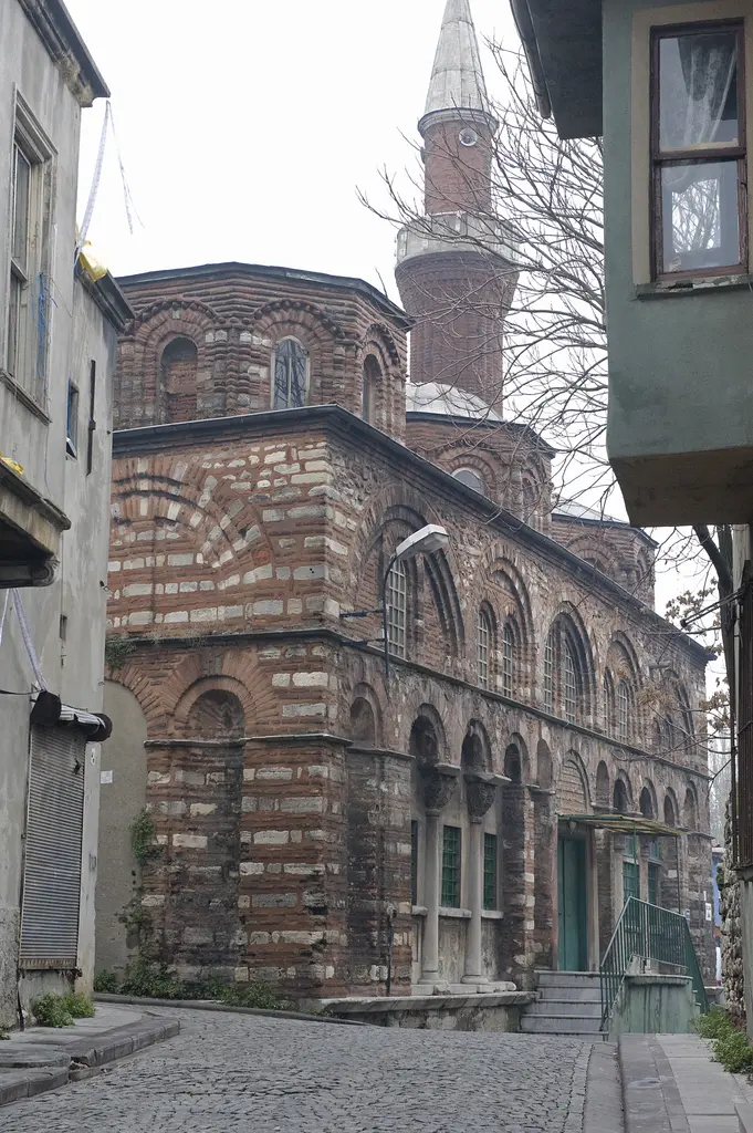 Vefa Kilise Camii'nin kuzeydoğu köşesi sisli bir kış gününde; solda gri sıvalı, sağda yeşil ahşap evin arasında kalan çokgen kubbe kasnağı, sağır kemerler ve minare.