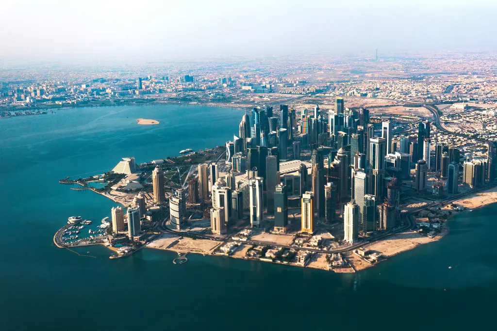 Doha'da havadan görünüm; denize uzanan kıyı şeridi, yan yana dizilmiş yapı adaları ve arkada dağılan gökdelenler.