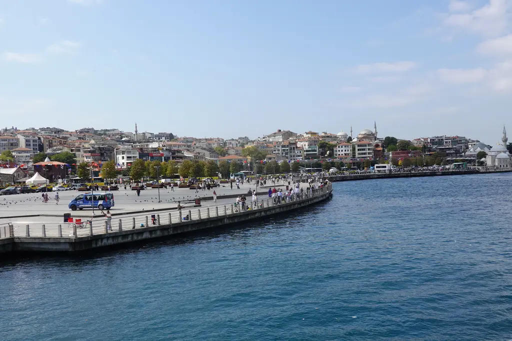 Üsküdar sahili; geniş taş döşeli meydan, deniz kenarı boyunca yürüyen insanlar ve yamaçlara yayılan binalar.