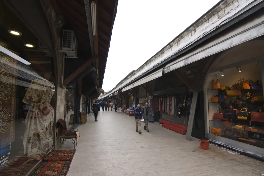 Sabah Arasta Çarşısı; henüz sakin sokak, iki yanda tuğla kemerli dükkânlar, ahşap sundurmalar ve uzakta yürüyen birkaç insan.