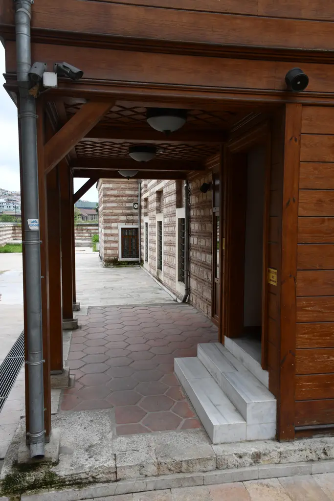Şah Sultan Camii'nin ahşap revakı; ahşap direkler ve tavan, mermer basamaklar, kapı ve uzanan taş döşeme.
